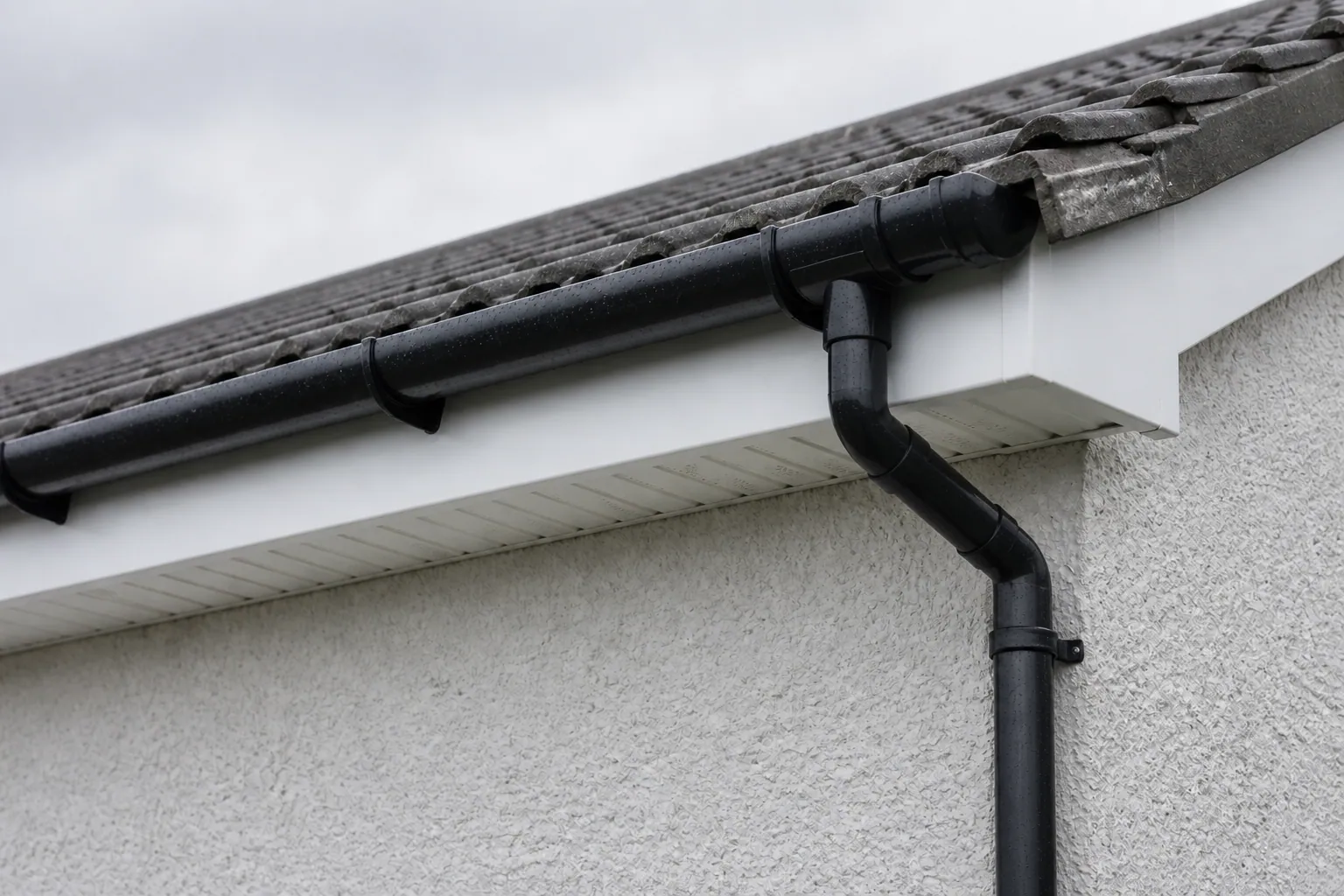 White fascia and ventilated soffit with a black gutter and downpipe beneath grey concrete roof tiles.