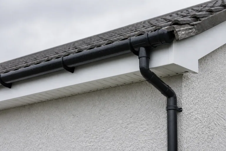 White fascia and ventilated soffit with a black gutter and downpipe beneath grey concrete roof tiles.