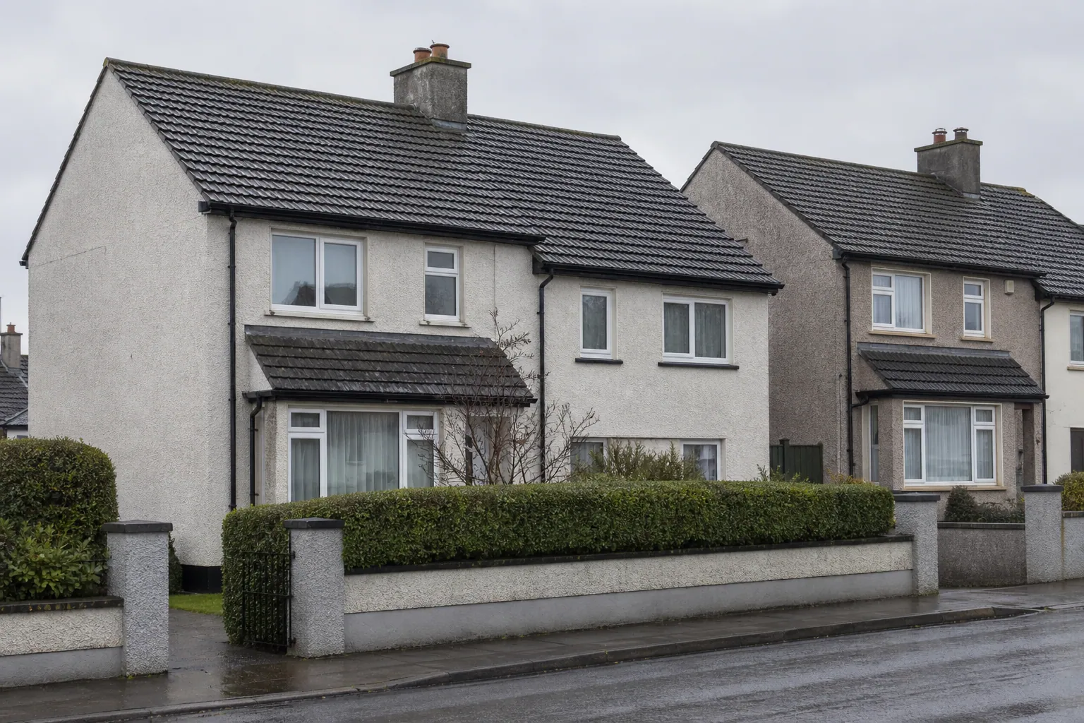 Irish-style rendered homes with dark tiled pitched roofs, chimneys and black gutters under an overcast sky.