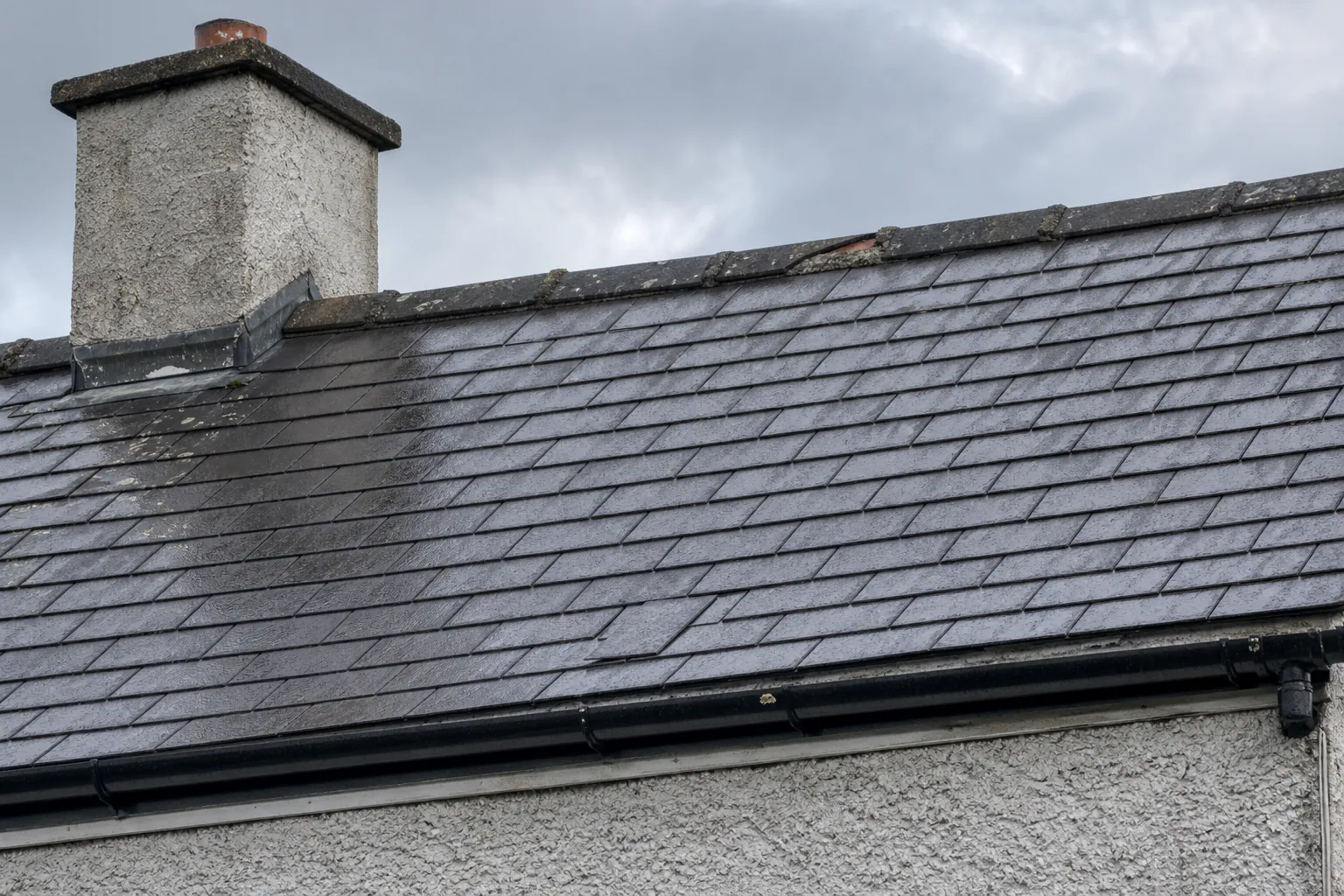 Ground-level view of a wet slate roof with a slipped slate and a small damaged area along the ridge.