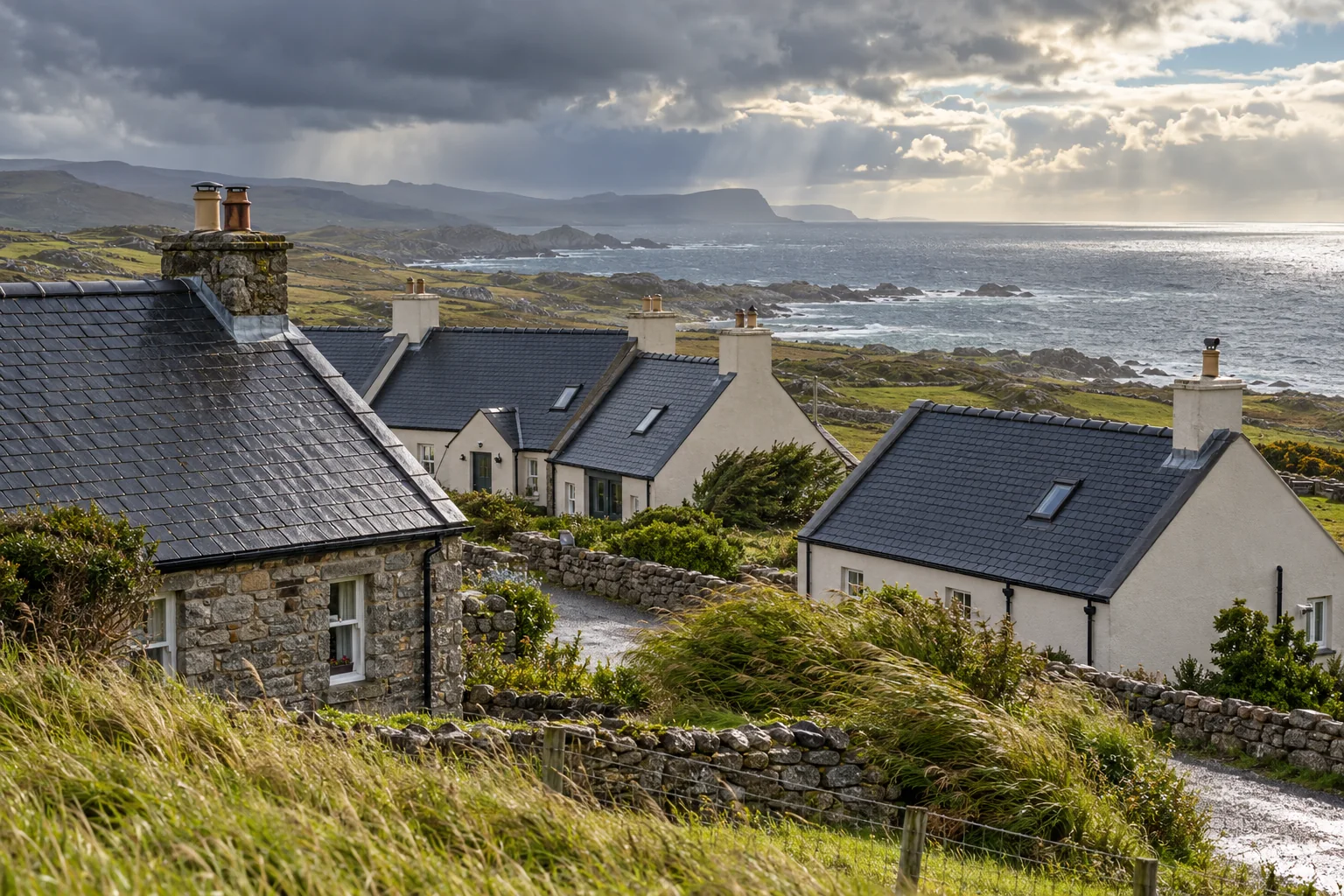 Rendered and stone Irish homes with dark slate roofs face an exposed Atlantic coastline under clearing rain.